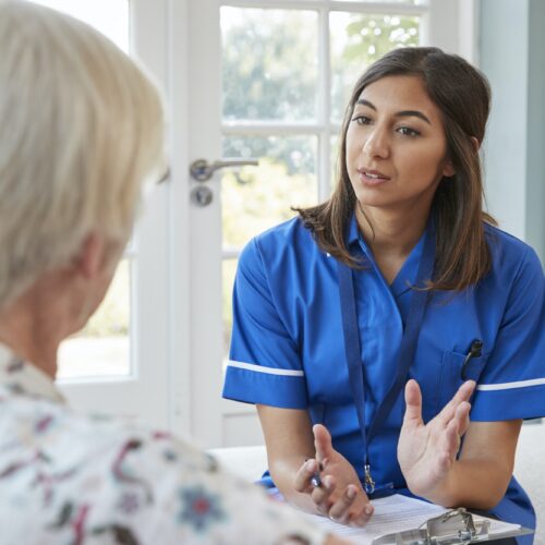 Senior woman talking to young care nurse on home visit